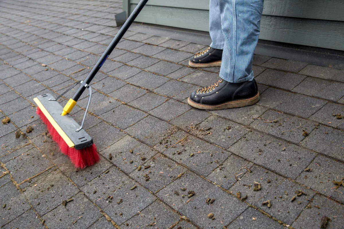 Brushing loosened moss down a shingle slope with a long-handled brush